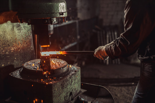 Caucasian Young Strong Blacksmith Working With Open Fire In Furnace. The Blacksmith Forging Hot Iron In Workshop