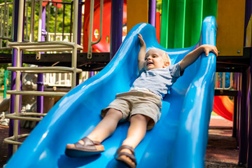 Little child boy playing on slide at park playground