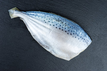 Ready-to-cook raw fresh pompano fish on a black stone slate background