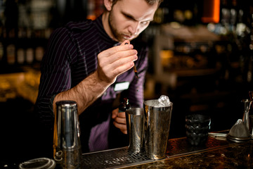 Bartender adding a brown essence from the pipette to an alcoholic drink in a steel shaker