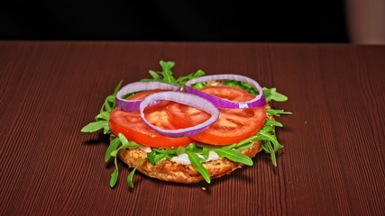 Craft burger is cooking on black background. Consist: sauce, arugula, tomato, red onion, bacon, red currant sauce, ricotta cottage fresh cheese, air bun and marble meat beef. Not made ideal. Looks