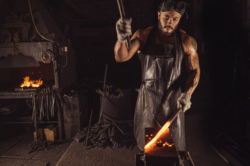 strong muscular brutal confident blacksmith man shaping red hot metal with hammer isolated in...