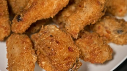 Cool beautiful fresh juicy cooked chicken wings in breading. Buffalo wings spread on food white plate in table. Very tasty and beautiful. Cooking with deep fryer fry machine.