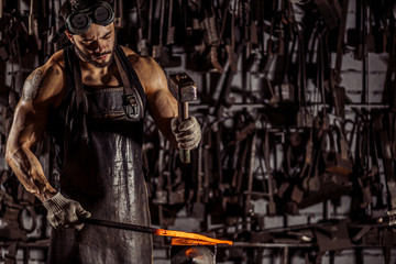 Fototapeta na wymiar blacksmith beat hot metal with hammer isolated in dark workshop space, wearing leather brown apron and having muscular body