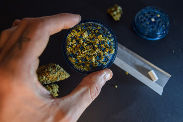 A man rolls a marijuana cigarette black background,paper, grinder and a marijuana dried flowers