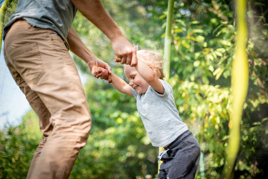 Little child with his dad playing on trampoline outdoor in backyard - Powered by Adobe