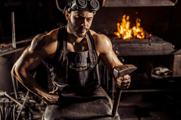 Fototapeta na wymiar muscular man work at workshop using hammer, wearing leather uniform and having strong body