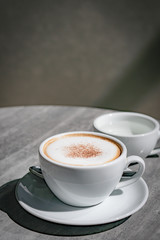 Hot coffee, hot tea  and flower vase with green leaves place on the marble table in early morning with copyspace, white cup and silver spoon.