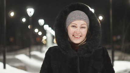 Pretty woman walking along the black fur coat. Outdoor. Girl walks on a winter night among the street lights of the city. Snow park with garlands. Beautiful sensual happy smile. © ivandanru