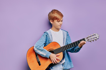 portrait of talented kid boy holding acoustic guitar and try to play on it, wearing casual clothes...
