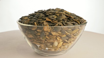 Nuts peeled pumpkin seed rotate are on a table in a plate. Snack in transparent dish on an isolated white background are spinning moving. Delicious and healthy protein-rich diet food.