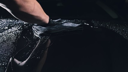 Using rag in palm of your hand, drops are removed from the car. Drop flow down the hood. Close up...