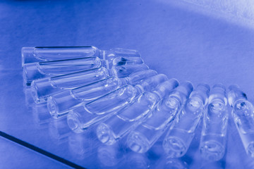 Glass medical ampoule vial for injection. Medicine is liquid sodium chloride with of aqueous solution in ampulla. Close up. Bottles ampule multicolor on background color and water. Human plasma.