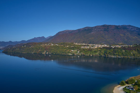 Aerial view of Lake Caldonazzo north of Italy. In the background the trees, Alps, blue sky. Reflection of mountains in water. Autumn season. Multi-colored palette of colors © Berg