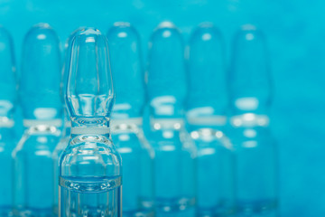 Glass medical ampoule vial for injection. Medicine is liquid sodium chloride with of aqueous solution in ampulla. Close up. Bottles ampule multicolor on background color and water. Human plasma.