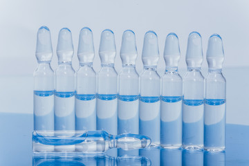 Glass medical ampoule vial for injection. Medicine is liquid sodium chloride with of aqueous solution in ampulla. Close up. Bottles ampule multicolor on background color and water. Human plasma.