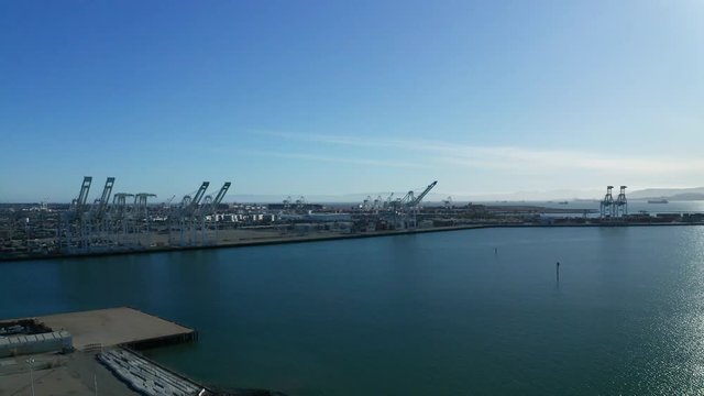A long pan across large shipping cranes and the bay waters as the sun shines.