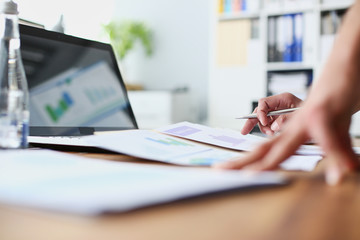 Male hands on the office desk. Young businessman holding a pen in hand and studies the results of sales represented on the graphics. Concept of office workplace.