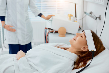 beautiful caucasian woman lying on bed in hospital, smile while her doctor examine her health status, using frontlet