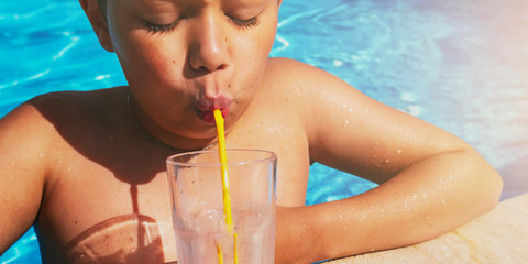 Beautiful teenager boy relaxing at swimming pool with cocktail. Kid having fun on summer vacation. Holiday and lifestyle concept