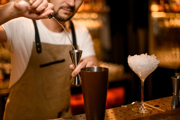 Bartender pours cocktail with bar spoon and jigger