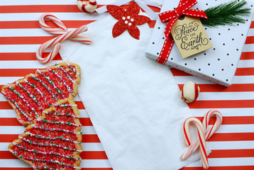 Christmas cookies and decor surround a white napkin on a cheerful red and white striped background. Top view, overhead flat lay design.