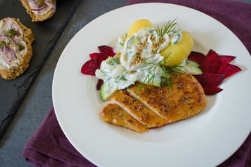 Food photography of a food dish with boiled potatoes, a vegetarian cutlet, beets and a cucumber, yogurt and dill salad on a schist table.