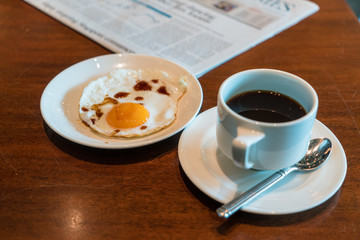 Black coffee on the table with fried egg and business newspaper.