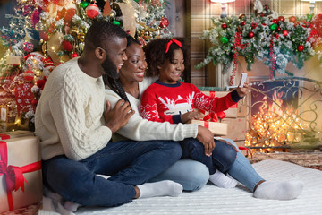 Little black girl taking selfie with parents near Christmas tree