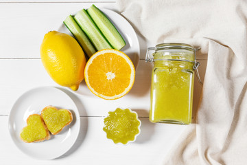 Homemade cucumber jam with lemon and heart-shaped toast on a white wooden background.