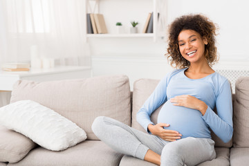Lovely pregnant woman embracing her belly at home