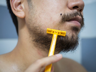 closeup man use yellow shaver shaving messy beard and mustache on his face in bathroom - 306732915