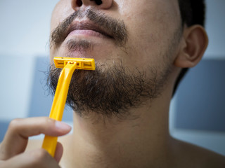 closeup man use yellow shaver shaving messy beard and mustache on his face in bathroom - 306732969