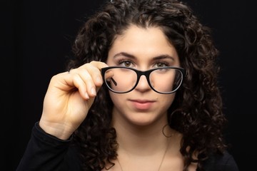 Close-up of a girl with black hair and brown eyes holding her glasses with one hand