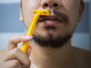 closeup man use yellow shaver shaving messy beard and mustache on his face in bathroom - 306732997