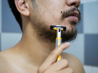 closeup man use yellow shaver shaving messy beard and mustache on his face in bathroom - 306733181