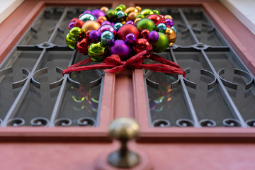 Door decoration of christmas balls with red ribbon at rustic house door at daytime.