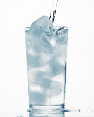 pouring water in a glass full of ice cubes, white background, blue toned object