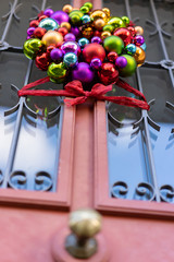 Door decoration of christmas balls with red ribbon at rustic house door at daytime.