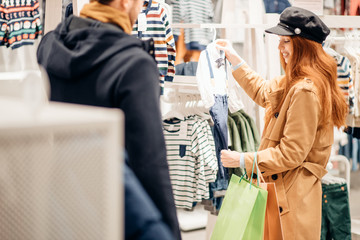 caucasian woman in search of clothes for future baby, pregnant woman with red hair in clothes store