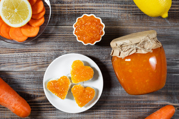 Homemade carrot jam with lemon in a glass jar on a dark brown wooden background.