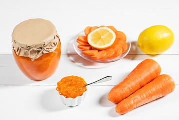 Homemade carrot jam with lemon in a glass jar on a white wooden background.