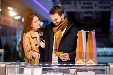 newly married couple, caucasian man and woman during shopping in mall, choose expensive jewelry for female, wearing coat and hugging man