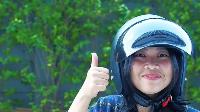A Young Woman fastening or Wearing her motorbike helmet with blur Fukien tea tree Carmona retusa green background - Zero accident concept