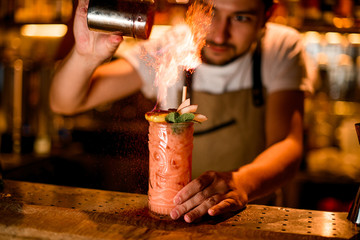Fototapeta na wymiar Male bartender sprinkles fired up alcohol drink