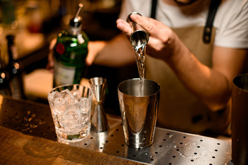 Bartender pouring alcohol drink from jigger to shaker