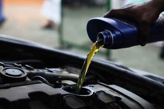 Mechanic pours motor oil into engine from blue plastic container