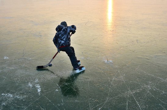 A child playing ice hockey on a frozen lake at sunset.