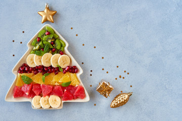  Christmas background with fruit salad in fir tree shaped plate and holiday decoration. Top view...