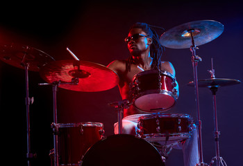 vigorous black man wearing eyeglasses emotionally playing drums isolated over neon lights in studio